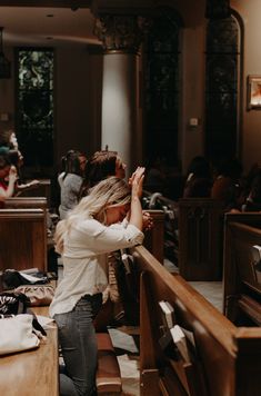 a woman kneeling down in front of pews with her hands up to her head