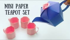 there is a paper teapot set with four cups next to it