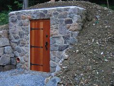 a stone building with a wooden door on top of it's side in the woods