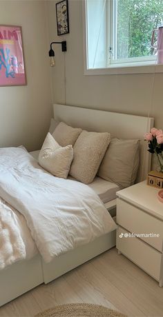 a white bed sitting in a bedroom next to a dresser with flowers on top of it