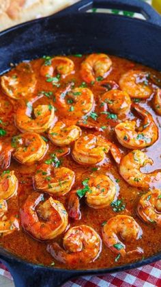 a skillet filled with shrimp and sauce on top of a checkered table cloth