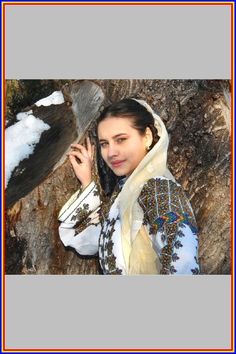 a woman in a white and blue dress standing next to a tree with snow on it