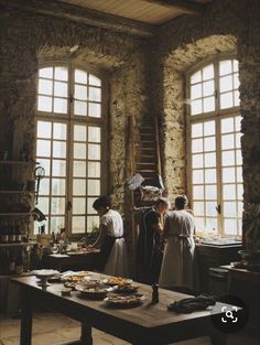 three people standing in front of two windows with food on the table next to them