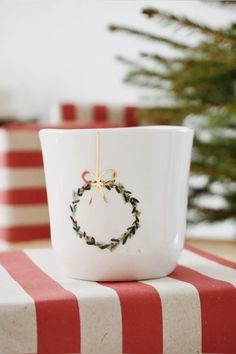 a coffee cup with a christmas wreath on the inside sits on a striped tablecloth