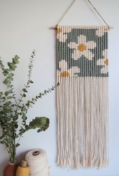 a wall hanging with flowers on it next to a potted plant and some yarn