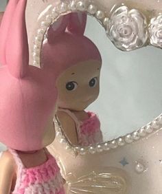 a small doll is standing in front of a mirror with pearls on it's head