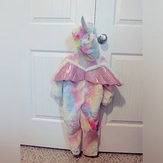 a stuffed unicorn is standing in front of a door wearing a pink and blue outfit