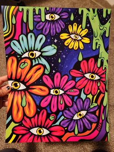 someone is holding up a colorful painting with flowers on the bottom and an eye in the middle