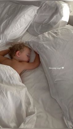 a young boy sleeping in a bed with white sheets