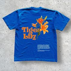 **Tiger Lily Graphic Tee** Bring a vibrant pop of color to your wardrobe with this bold blue tee, featuring a striking orange tiger lily graphic and "Tiger Lily" text. Crafted from 100% cotton, it's as comfortable as it is stylish. The shirt showcases environmentally friendly white direct injection and black thermal offset printing, making it both eco-conscious and durable. 👕 Material: 100% Cotton   🎨 Design: Bold Orange Tiger Lily Graphic with "Tiger Lily" Text   ⚖️ Weight: Approx 230G   📏 S Casual Streetwear Floral Print Tops, Casual Floral Print Tops For Streetwear, Casual Floral Print T-shirt For Streetwear, Short Sleeve Tiger Print T-shirt For Summer, Tiger Print Short Sleeve T-shirt For Summer, Relaxed Fit Floral Print T-shirt For Streetwear, Streetwear Short Sleeve Floral Print T-shirt, Streetwear Floral Print Short Sleeve T-shirt, Short Sleeve Floral Print Streetwear T-shirt