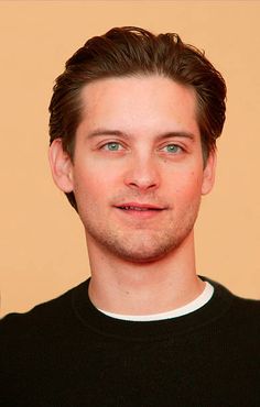 a close up of a person wearing a black shirt and looking at the camera with a smile on his face