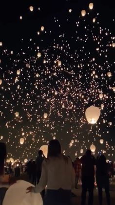 people are looking at lanterns floating in the night sky with white paper lanterns on them