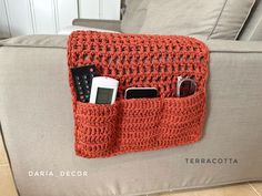 an orange crocheted purse with cell phones in it sitting on a couch next to a remote control