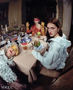 two women sitting at a table with plates and cups in front of them, one wearing a clown mask