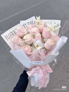 a bouquet of pink and white flowers is being held by someone's hand on the street