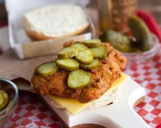 a sandwich with pickles and cheese on it sitting on top of a red and white checkered table cloth