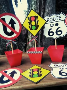 various road signs are displayed on a table with potted plants and trees in the background