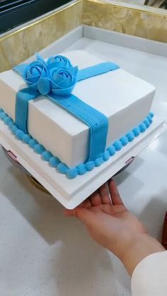 a person holding a square cake with blue ribbon on it