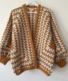 an orange and white crocheted sweater hanging on a hanger