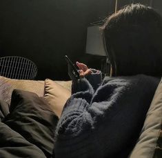 a woman sitting on top of a bed holding a cell phone in her hand and looking at the screen