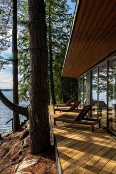 two chaise lounges are on the deck overlooking the water and trees in the foreground