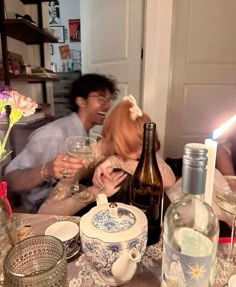 two people sitting at a table with wine bottles and glasses in front of them,