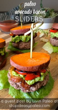 four hamburgers with lettuce and tomatoes on a cutting board next to dipping sauce