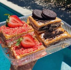 a person holding up a plastic container with desserts in it and two cookies on top