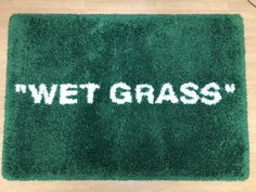 a green rug with the words wet grass written in white across it on a wooden floor