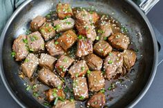 some meat is being cooked in a pan on the stove with green onions and sesame seeds