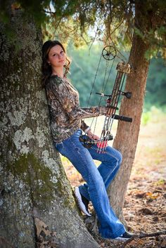 a woman leaning against a tree with her bow