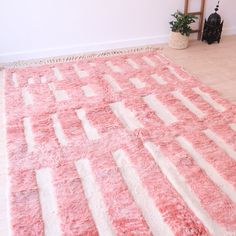 a pink and white area rug on the floor in front of a chair with a plant