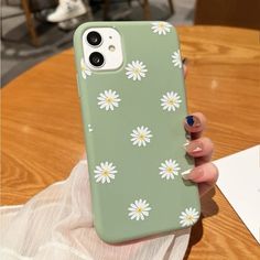 a woman holding up her phone case with daisies on it