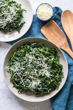 two bowls filled with spinach and cheese on top of a blue towel next to wooden spoons