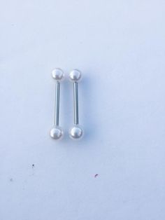 two white pearls are attached to the end of a pair of screws on a white surface