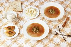 four white plates with food on them sitting on a table cloth covered in gold and white designs