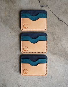 three leather wallets sitting next to each other on a concrete floor, one with blue and tan trim