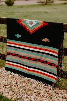 a blanket is hanging on a fence in the middle of some rocks and gravel, with a grassy field behind it