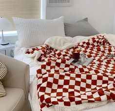 a red and white blanket sitting on top of a bed next to a couch with pillows