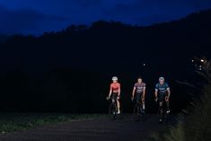 three people riding bikes on a road at night