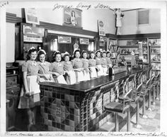 an old black and white photo of women in uniforms standing at a counter with aprons