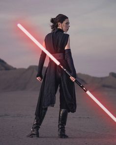 a woman standing in the desert holding two lightsabes