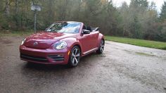 a red convertible car parked on the side of a road in front of some trees