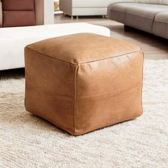 a brown leather ottoman sitting on top of a white rug in a living room next to a couch