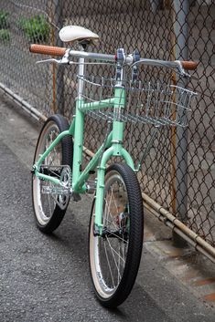 a green bike parked next to a chain link fence with a basket on the front