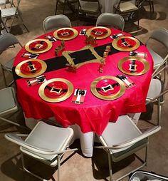 a red table topped with lots of gold plates and place settings on top of it