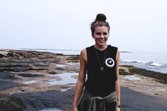 a woman is standing on the rocks by the ocean with her hand in her pocket