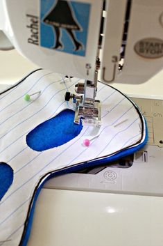 the sewing machine is on top of the white fabric with blue and black stitching