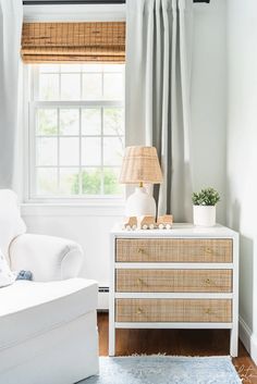 a living room with a white couch and a wicker dresser in front of a window