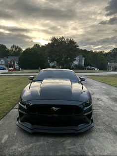 a black car parked on top of a cement road next to a lush green field